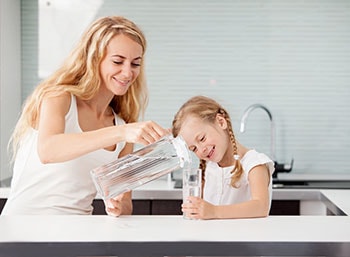 Child with Mother Drinking Water from Glass in Kitchen