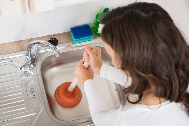 woman using plunger on kitchen sink drain.