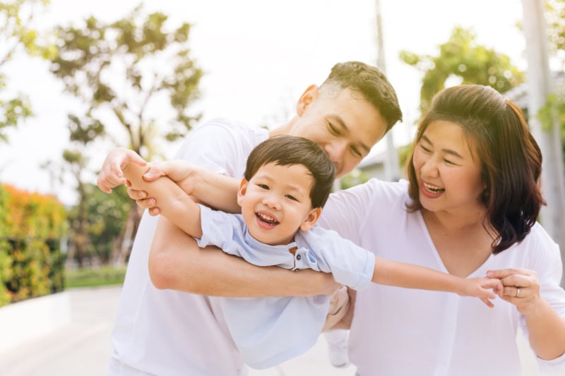 Family having fun and carrying a child in public park.
