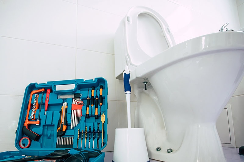 Close up photo of ceramic bowl toilet in domestic bathroom with a box of tools.